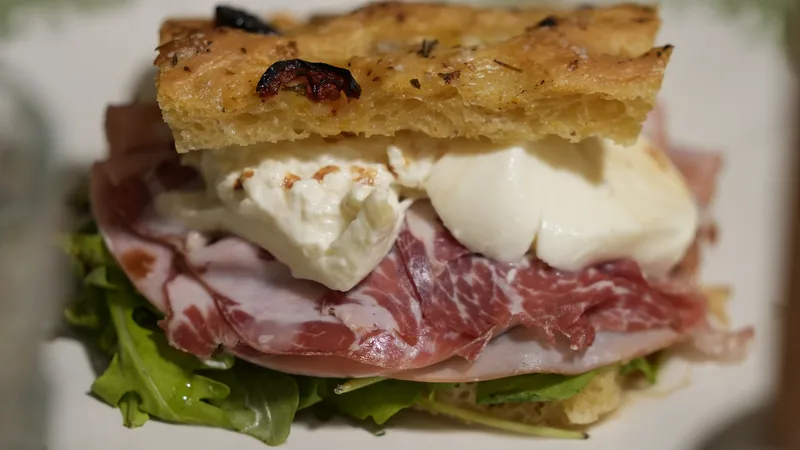 A focaccia sandwich with creamy cheese, sliced meats and greens.